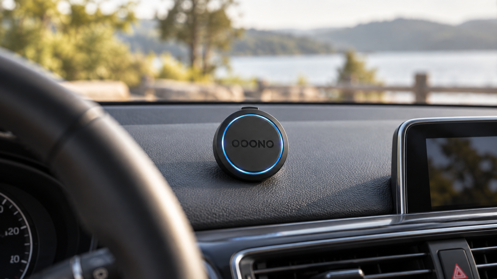 Schwarzer OOONO Co-Driver NO2 mit blauem LED-Ring auf dem Armaturenbrett eines Autos, im Hintergrund eine unscharfe Seenlandschaft